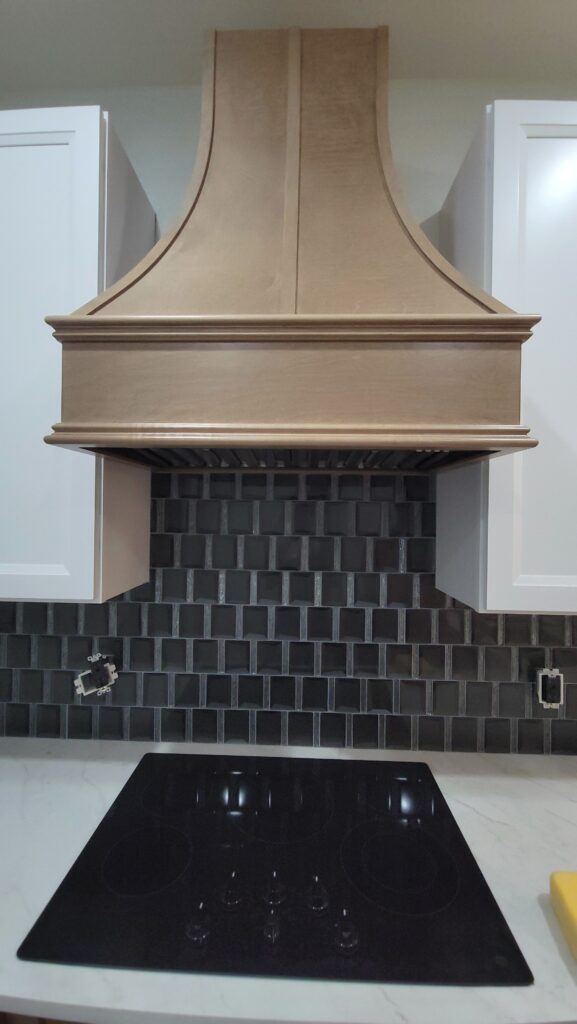 Glass tile kitchen backsplash beneath a wood range hood between white cabinets
