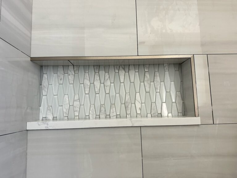 Shower niche with a glass mosaic back, metal edge trim and a marble-look shelf, set in large-format wall tile before grouting