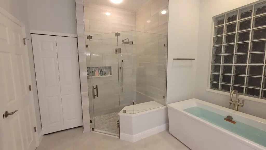 Renovated Naples bathroom with large-format porcelain tile, frameless glass shower, built-in bench, and freestanding bathtub.