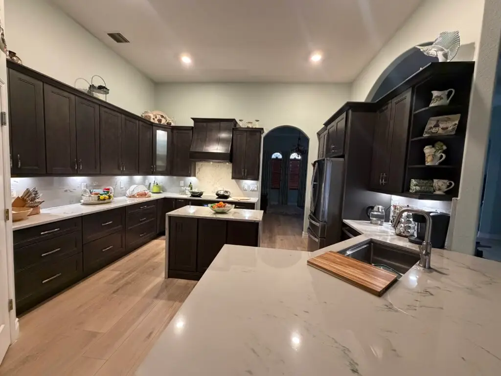 Completed Cape Coral kitchen with smoky gray cabinetry, custom wood range hood, quartzite island, and full-height stone backsplash