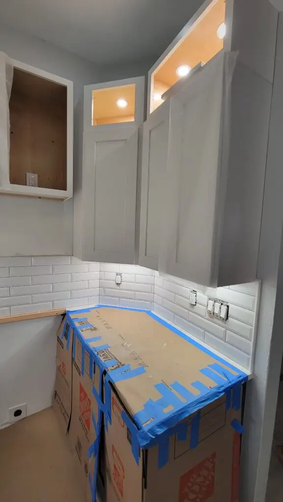 Kitchen renovation in progress with white shaker upper cabinets and a white subway tile backsplash being installed in a Naples home