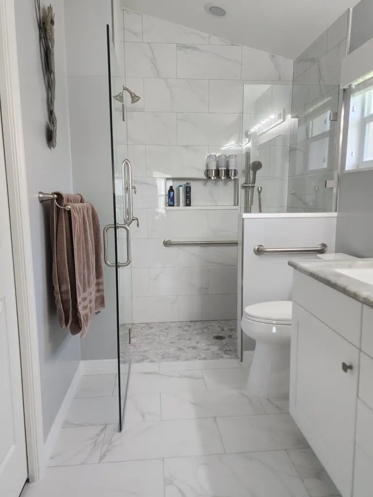 Completed walk-in shower with frameless glass, marble-look porcelain wall tile, recessed niche, and natural-stone floor in North Fort Myers