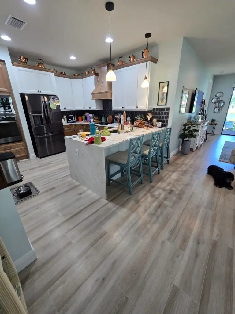 Completed Pletcher Residence kitchen in Ave Maria, Florida, featuring Oxford White and Oxford Toffee cabinets, quartz countertops, decorative backsplash, and wood-look porcelain tile flooring.