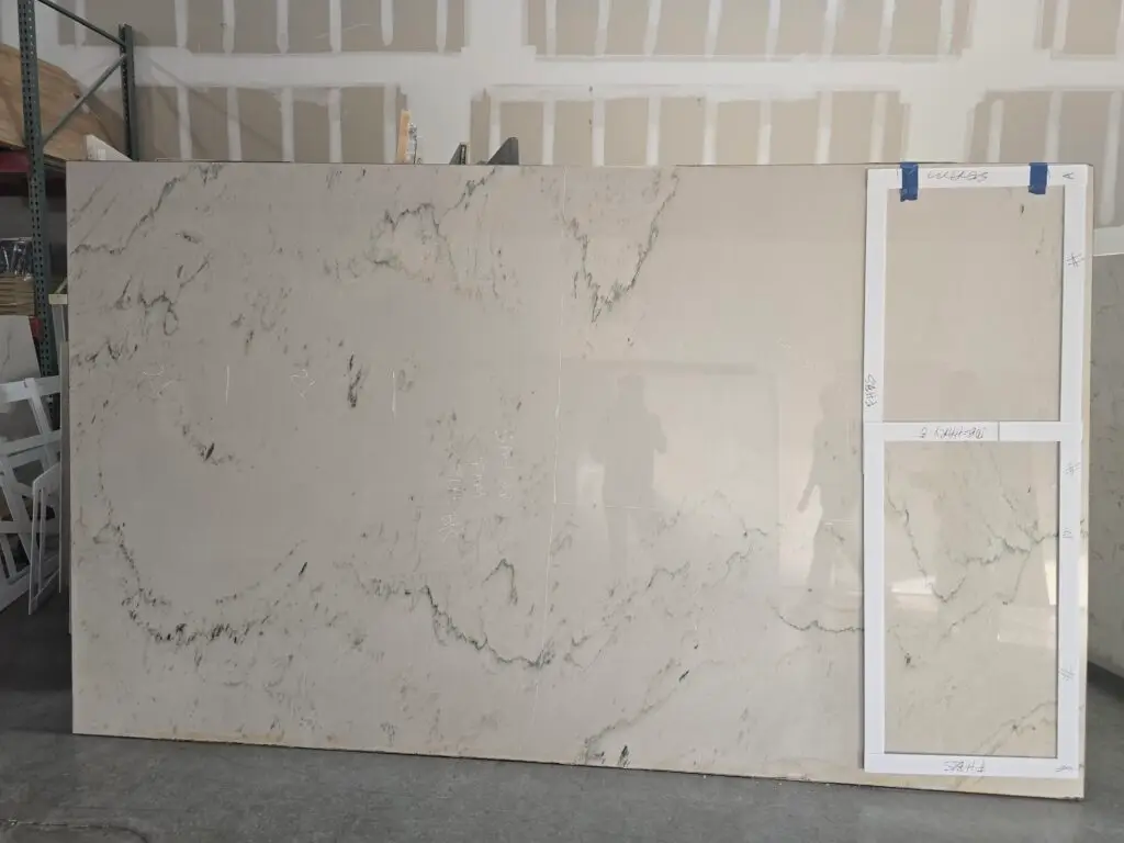 Quartzite slab with gray veining and taped templates positioned to plan countertop cuts