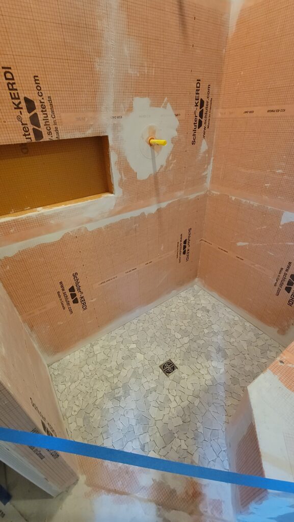 Schluter KERDI waterproofing membrane on shower walls with recessed niche and mosaic tile floor in Naples, Florida.